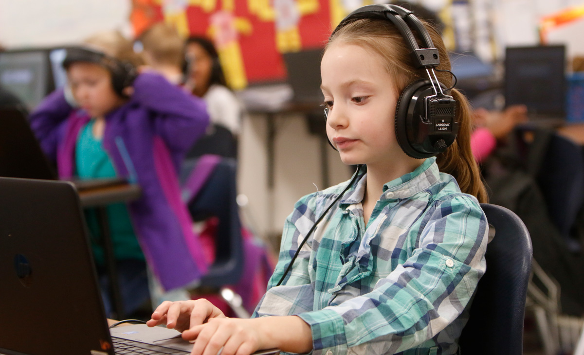 Photo of a student using a laptop, while wearing headphones